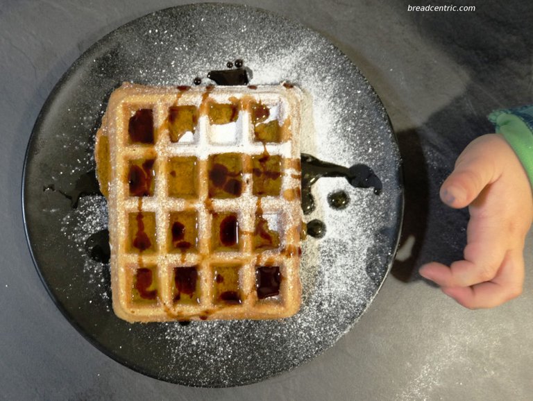 Waffles with icing sugar, maple sirup and sour cherries preserve juice